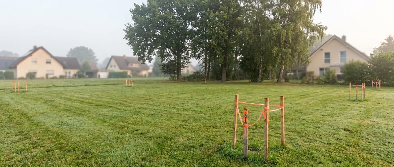 Unbebautes Baugrundstück mit Vermessungspflöcken im Morgenlicht